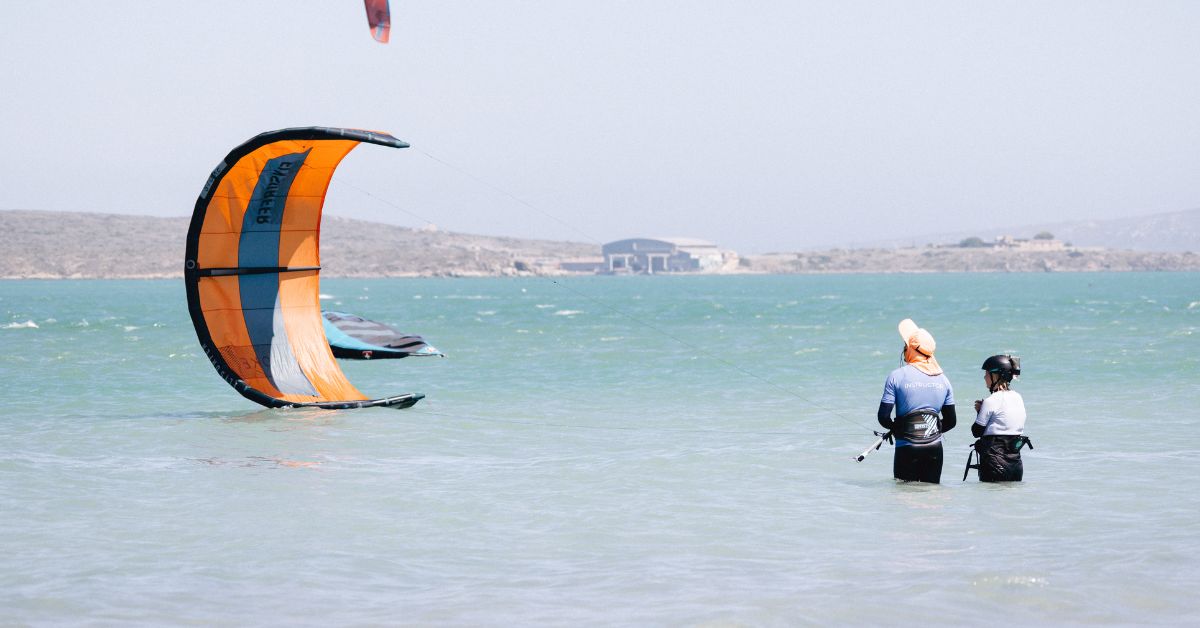Teacher learning student how to kitesurfing in shallow water with an organge kite.
