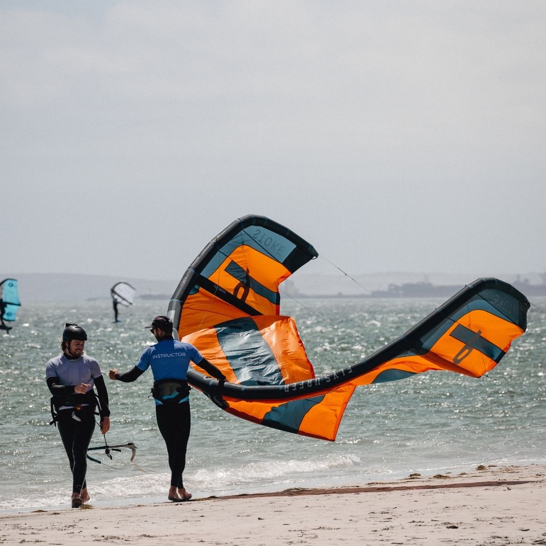 Student and instructor with an orange Flysurfing  kite on main beach in South Africa Langebaan.