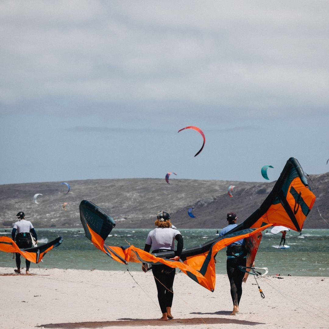People with kites on main beach with a kite flying in the background in South Africa