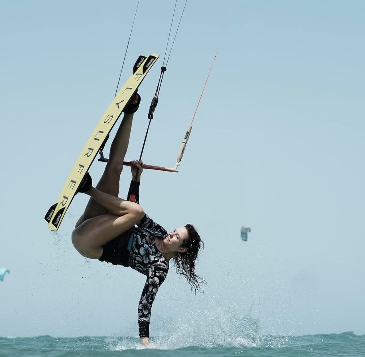 Kitesurfer grabbing her board mid-air during an advanced trick above turquoise water