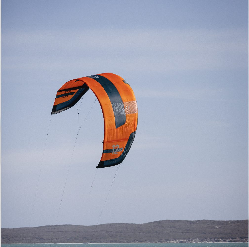 Orange kitesurfing kite from Flysurfer flying in a cloudy sky above the water in Sharkbay Langebaan
