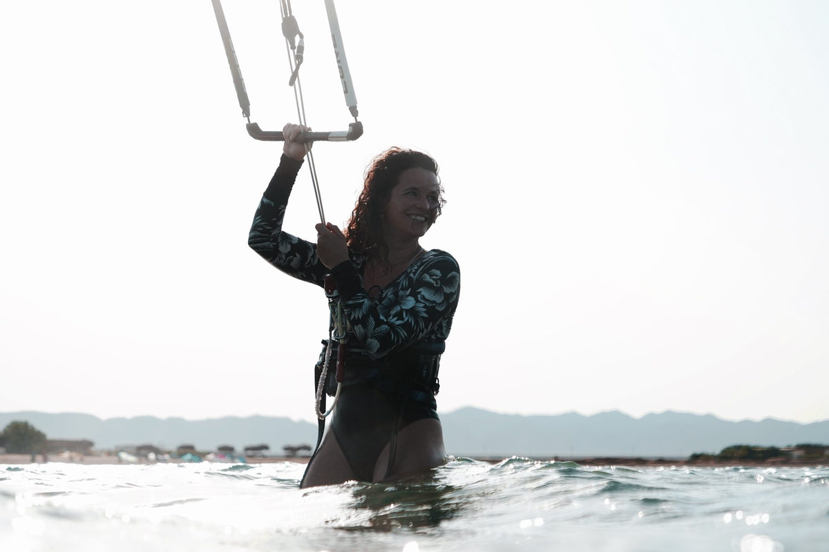 Smiling kitesurfer standing waist-deep in the water holding the kite  in the air
